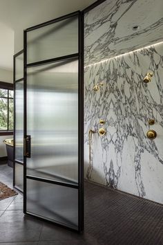 an open glass door leading to a bathroom with marble walls and flooring in the background