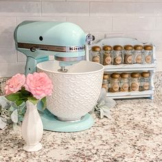 a blue mixer sitting on top of a kitchen counter next to a vase with flowers