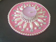 a pink candle sitting on top of a table next to a glass container filled with pearls