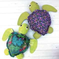 two stuffed animals made to look like turtles on a white wooden surface with flowers and leaves