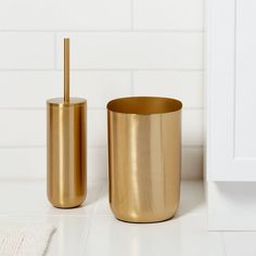 two gold bathroom accessories sitting on a white counter top next to a toilet brush and soap dispenser