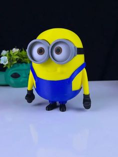 a yellow and blue minion with big eyes sitting in front of a potted plant