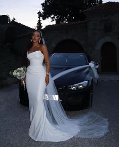 a woman standing next to a car wearing a wedding dress