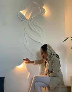 a woman sitting on top of a white bench next to a wall mounted with lights