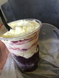 a person holding a spoon over a dessert in a plastic cup with whipped cream and blueberries