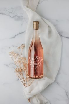 a bottle of pink wine sitting on top of a white cloth next to some dried flowers