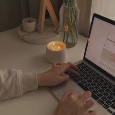 a woman is typing on her laptop with a candle in front of her and a vase full of flowers behind her