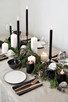 a table topped with candles and plates covered in greenery next to pineconis