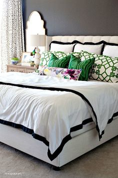 a white bed topped with lots of pillows next to a night stand and window sill