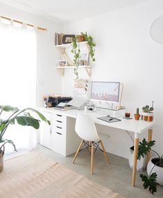 a white desk sitting in front of a window next to a potted plant on top of a wooden table