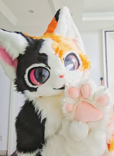 a large stuffed animal cat with big eyes and paws on it's chest, standing in front of a wall