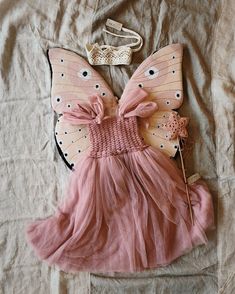 a pink dress is laying on a bed with a butterfly wings and flower in it