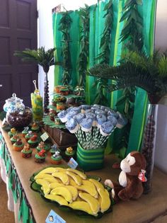 a table topped with bananas and cupcakes next to a green drapes curtain