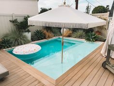 an umbrella sitting on top of a wooden deck next to a swimming pool in a backyard