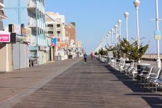 the boardwalk is lined with empty chairs and people walking on the sidewalk next to it