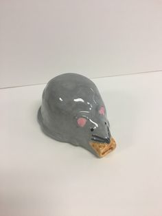 a gray ceramic animal head with pink eyes on a white surface, next to a piece of bread