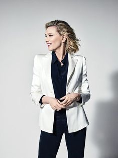 a woman in a white jacket and black shirt posing for the camera with her hands on her hips