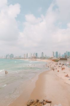 the beach is crowded with people and buildings in the background, as well as blue water