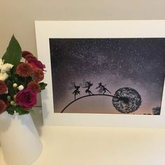 a white vase filled with red flowers next to a painting on top of a table