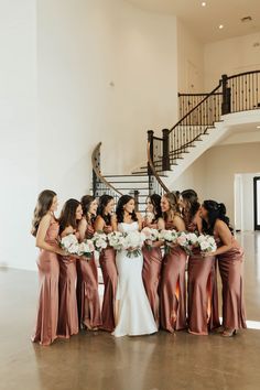 a group of women standing next to each other in front of a stair case holding bouquets