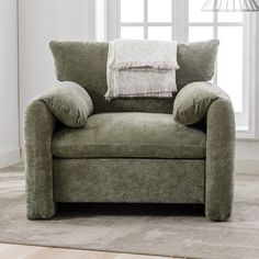 a green chair with two pillows on it in front of a window and rugs