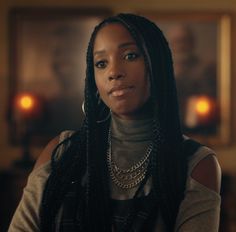 a woman with long braids standing in front of a candle lit room and looking at the camera