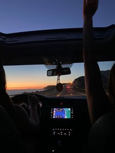 two people driving in the back seat of a car at sunset with their hands up