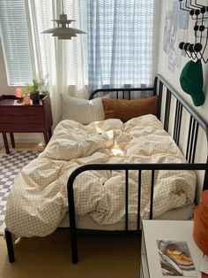 an unmade bed in a bedroom with blue and white checkered curtains, black metal frame