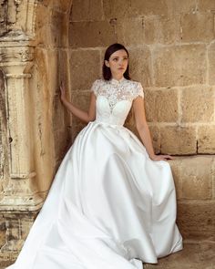 a woman in a white wedding dress leaning against a stone wall with her hand on her hip