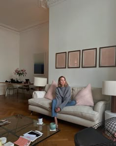 a woman sitting on top of a couch in a living room next to a coffee table