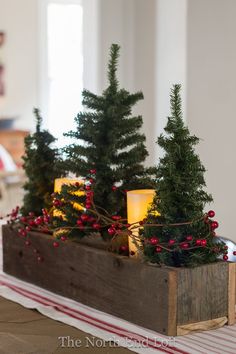 a wooden box filled with christmas trees on top of a table next to a candle