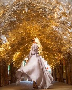 a woman in a long white dress is walking through the trees with lights on them