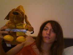 a woman sitting on a bed with a stuffed dog in front of her, holding up a toy