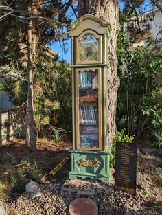 a grandfather clock sitting next to a tree with books on it's shelves in the park