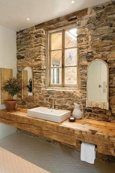 a bathroom with stone walls and wooden counter tops, along with a large white sink