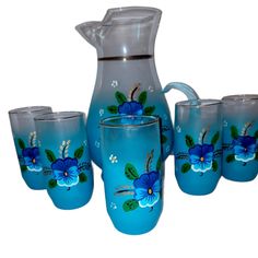 a pitcher and four glasses with blue flowers painted on them