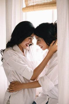 two women standing next to each other in front of a window