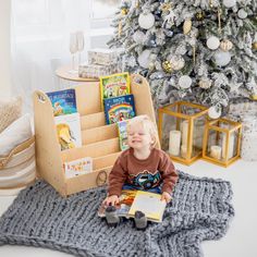 a toddler sitting in front of a christmas tree holding a book and looking at the camera