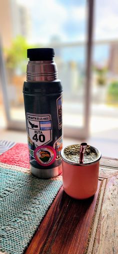 a coffee cup sitting on top of a wooden table next to a canister filled with liquid