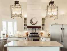 a kitchen with two chandeliers hanging from the ceiling and an island in front of it