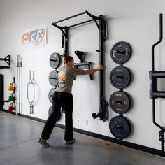 a woman is working on a wall mounted power rack in a crossfit gym