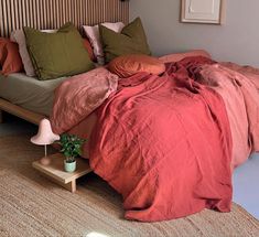 a bed with red sheets and pillows on top of it next to a night stand