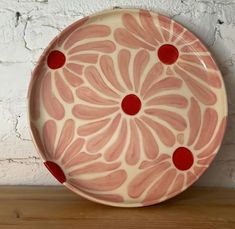 a pink and red plate sitting on top of a wooden table next to a white brick wall