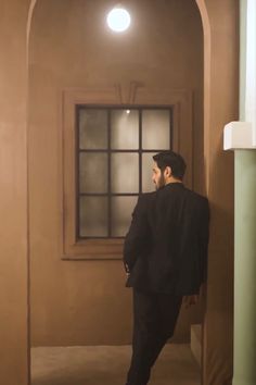 a man in a black suit is standing by a door and looking out the window