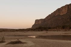 there is a small pond in the middle of the desert with mountains in the background