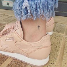 a woman's foot with a small cross tattoo on her left ankle and pink sneakers