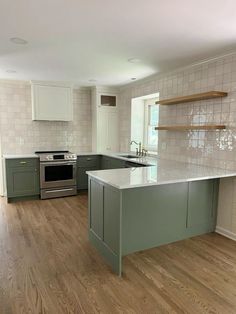 an empty kitchen with wood floors and green cabinets, white tile backsplash and stainless steel appliances