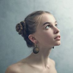 a woman with braids and earrings looks up into the sky while standing in front of a wall