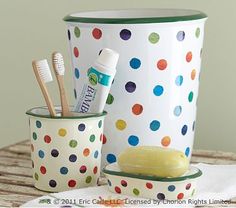 polka dot cups with toothbrushes, soap and toothpaste are on a table