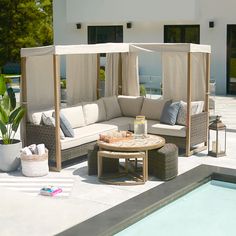 an outdoor living area with couches and tables next to a swimming pool in front of a house